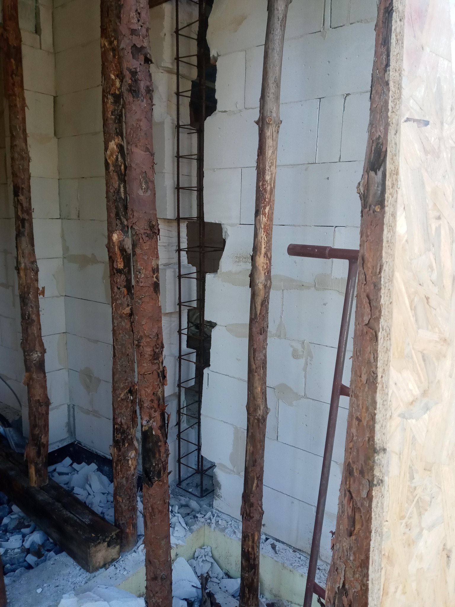 Wnętrze w trakcie budowy z widocznymi bloczkami, zbrojeniem w otworze, drewnianymi stemplami podpierającymi konstrukcję i gruzem na podłodze.