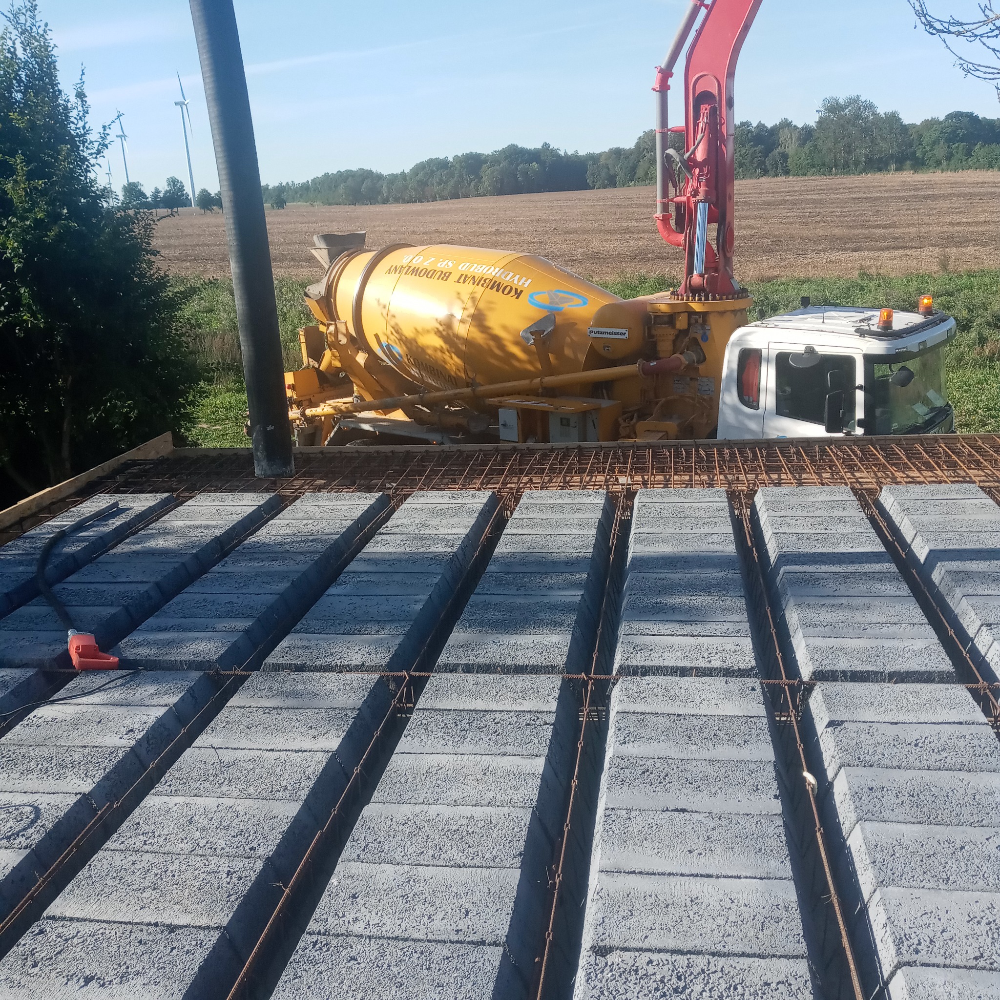 Wylewka stropu Teriva z betoniarki na budowie w Wieleniu, widoczne bloczki betonowe, stalowe pręty zbrojeniowe i rura do podawania betonu.