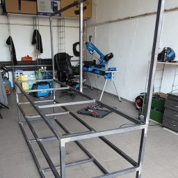 LIONTECH Jakub Kiedrowski - Szkielet metalowej konstrukcji w warsztacie, widoczne spawy, narzędzia i maszyny do obróbki metalu w tle.