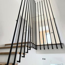 Harfa ze stalowych rurek fi 25x2 mm, zamontowana do boku schodów. Dla stabilności mocowana jest do boku stopnia i do sufitu na górze. Całość wykończona czarną, chropowatą farbą proszkową. Taki design tworzy nowoczesny kontrast z drewnianymi stopniami.