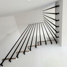 Harfa ze stalowych rurek fi 25x2 mm, zamontowana do boku schodów. Dla stabilności mocowana jest do boku stopnia i do sufitu na górze. Całość wykończona czarną, chropowatą farbą proszkową. Taki design tworzy nowoczesny kontrast z drewnianymi stopniami.