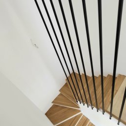 Harfa ze stalowych rurek fi 25x2 mm, zamontowana do boku schodów. Dla stabilności mocowana jest do boku stopnia i do sufitu na górze. Całość wykończona czarną, chropowatą farbą proszkową. Taki design tworzy nowoczesny kontrast z drewnianymi stopniami.