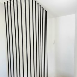 Harfa ze stalowych rurek fi 25x2 mm, zamontowana do boku schodów. Dla stabilności mocowana jest do boku stopnia i do sufitu na górze. Całość wykończona czarną, chropowatą farbą proszkową. Taki design tworzy nowoczesny kontrast z drewnianymi stopniami.