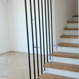 Nowoczesne schody z drewnianymi stopniami i czarną, minimalistyczną balustradą z pionowych rurek, mocowanych do stopnia i sufitu, na tle jasnego wnętrza.