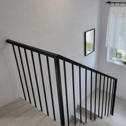 Balustrada z pochwytem 40x40 mm i wypełnieniem 15x15 mm. Tralki mocowane bezpośrednio do ściany, bez dolnego profilu, nadają konstrukcji lekkości. Całość dopełnia dolna harfa z profilu 15x15 mm, mocowana do boku.