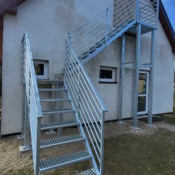 LIONTECH Jakub Kiedrowski - Zewnętrzne schody metalowe z balustradą, ocynkowane ogniowo, prowadzące do drzwi na piętrze budynku. Stopnie z kraty WEMA, filary i słupki z metalowych profili.