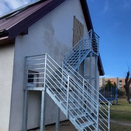 LIONTECH Jakub Kiedrowski - Zewnętrzne schody metalowe z balustradą, ocynkowane ogniowo, prowadzące do wejścia na piętro budynku. Stopnie z kraty WEMA, słupki i wypełnienie balustrady z profili.