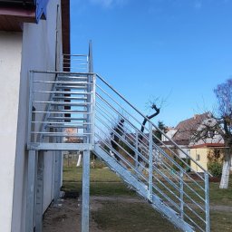 LIONTECH Jakub Kiedrowski - Zewnętrzne schody metalowe z balustradą, ocynkowane ogniowo, prowadzące do budynku. Stopnie z kraty WEMA, słupki i wypełnienie balustrady z profili stalowych.