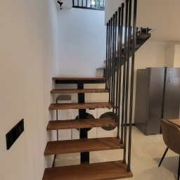 LIONTECH Jakub Kiedrowski - Nowoczesne schody metalowe z drewnianymi stopniami i balustradą z pionowych prętów, centralna belka, ukryte spawy, malowanie proszkowe, widok z dołu.
