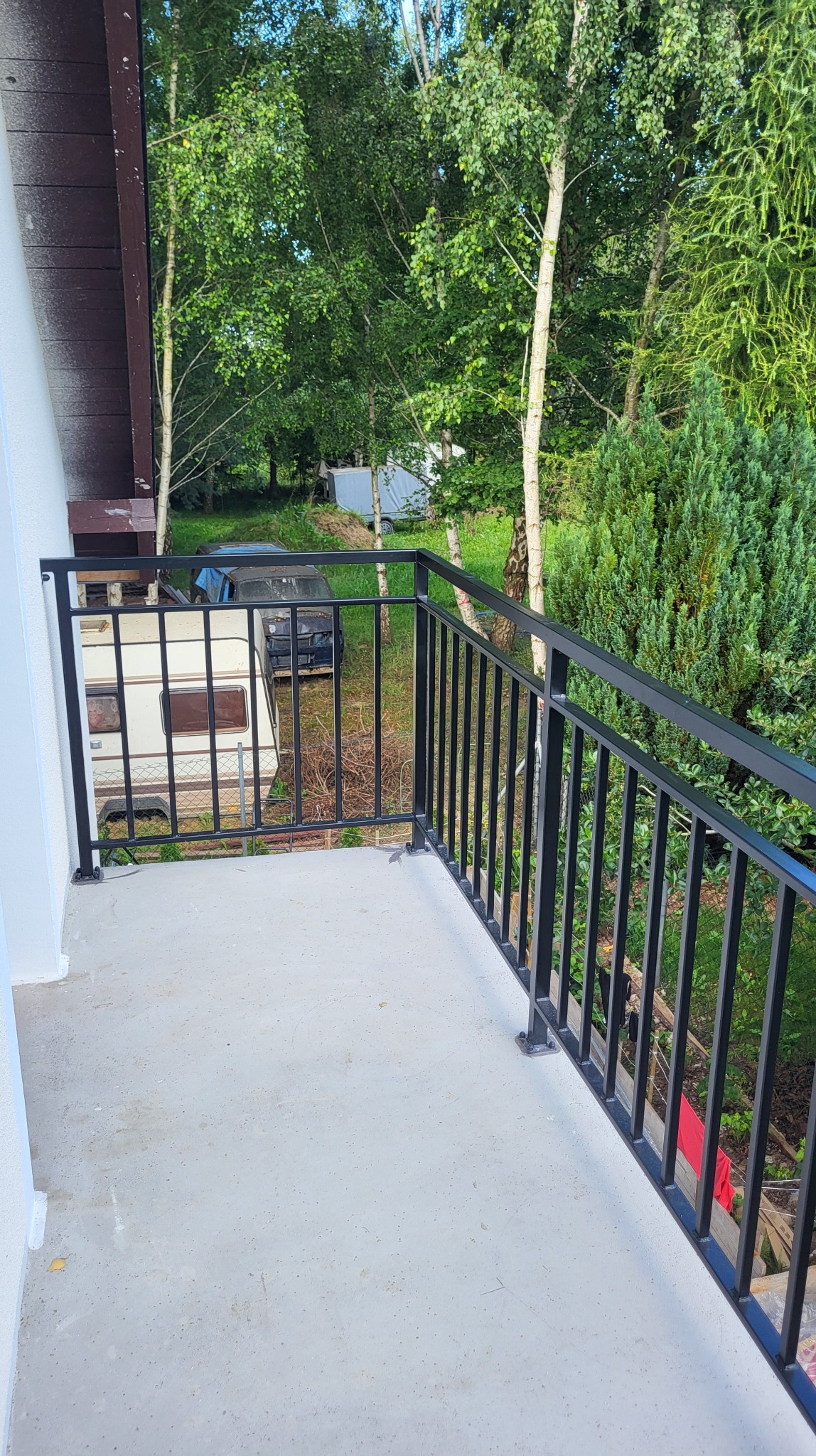 Czarna, metalowa balustrada balkonowa z profilami 40x40 i 20x20 mm, pomalowana proszkowo na mat, z widokiem na zieleń i przyczepę kempingową w tle.