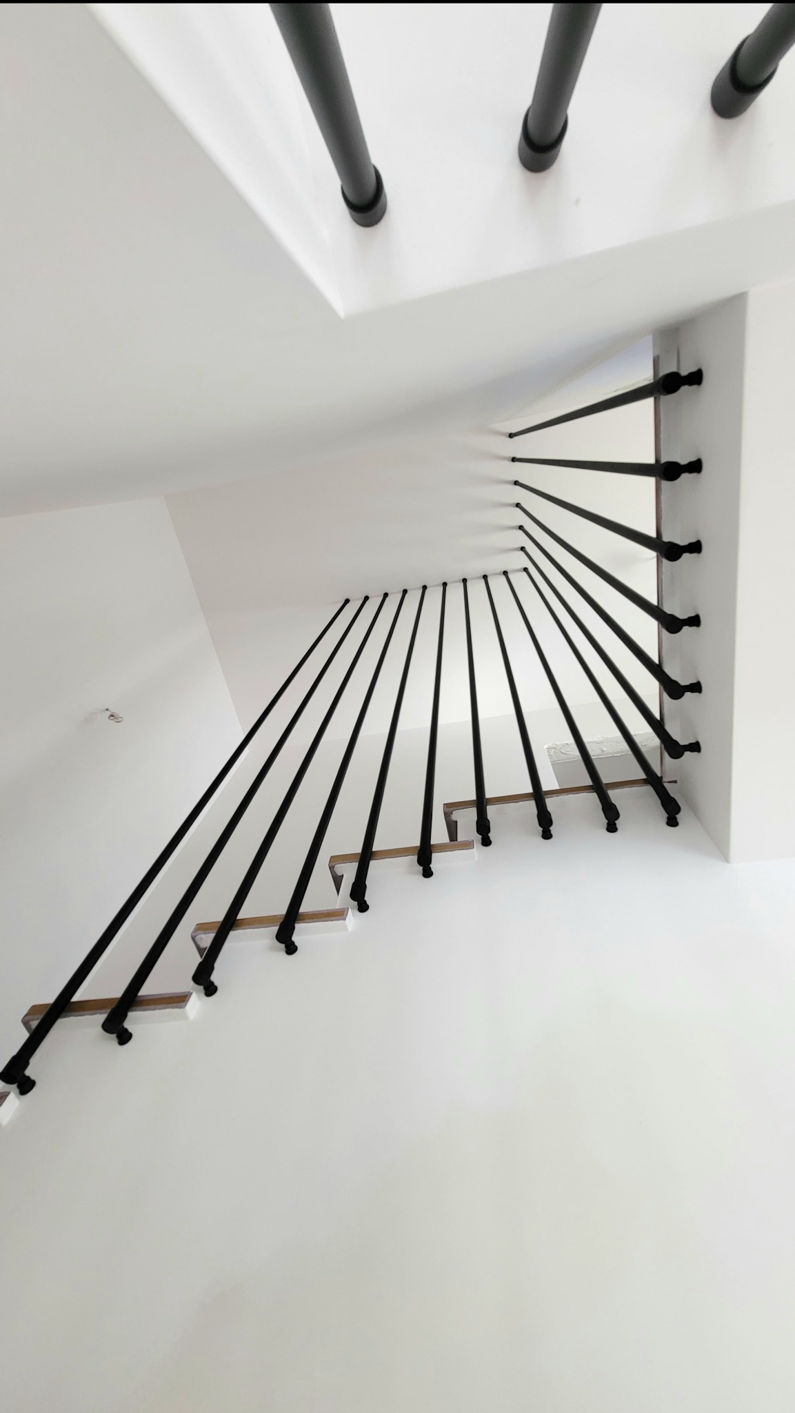 Nowoczesne schody z drewnianymi stopniami i czarnymi, stalowymi rurkami tworzącymi balustradę, mocowanymi do boku stopnia i sufitu. Minimalistyczny design.