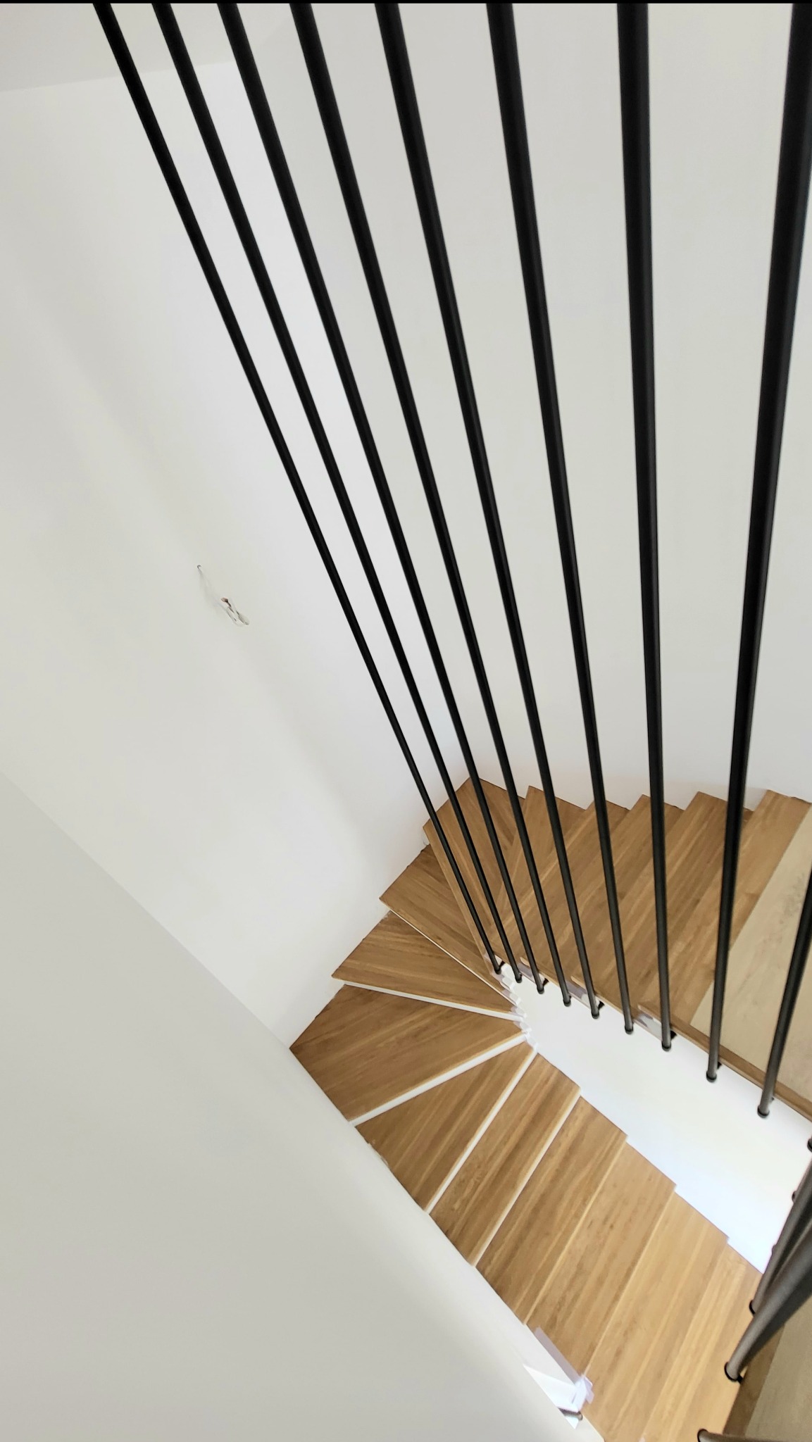 Spiralne schody z drewnianymi stopniami i minimalistyczną, czarną poręczą z rurek, widziane z góry. Nowoczesny design i kontrast materiałów.