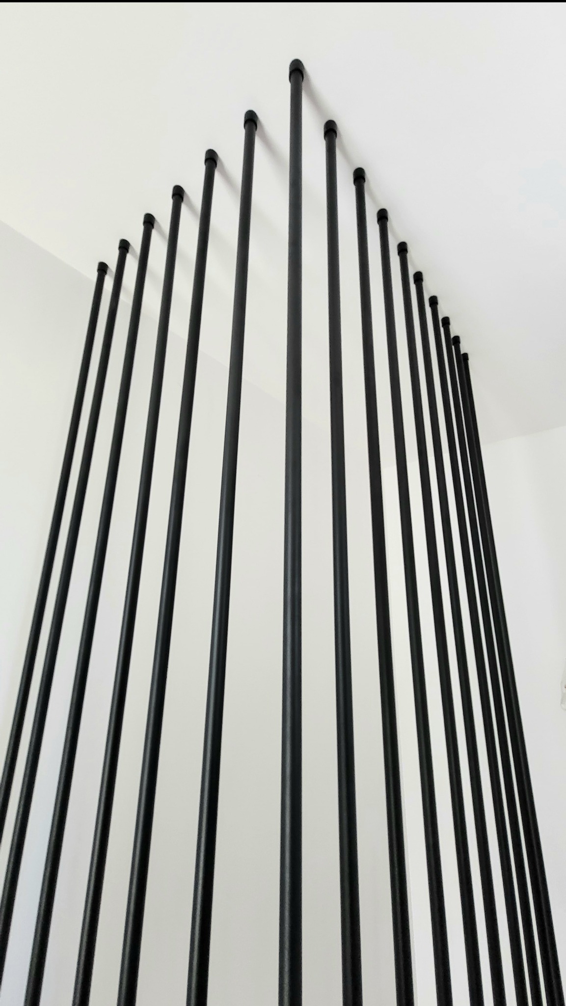 Stalowa konstrukcja z czarnych rurek tworząca nowoczesny design, zamocowana pomiędzy bokiem schodów a sufitem. Minimalistyczny detal architektoniczny we wnętrzu.