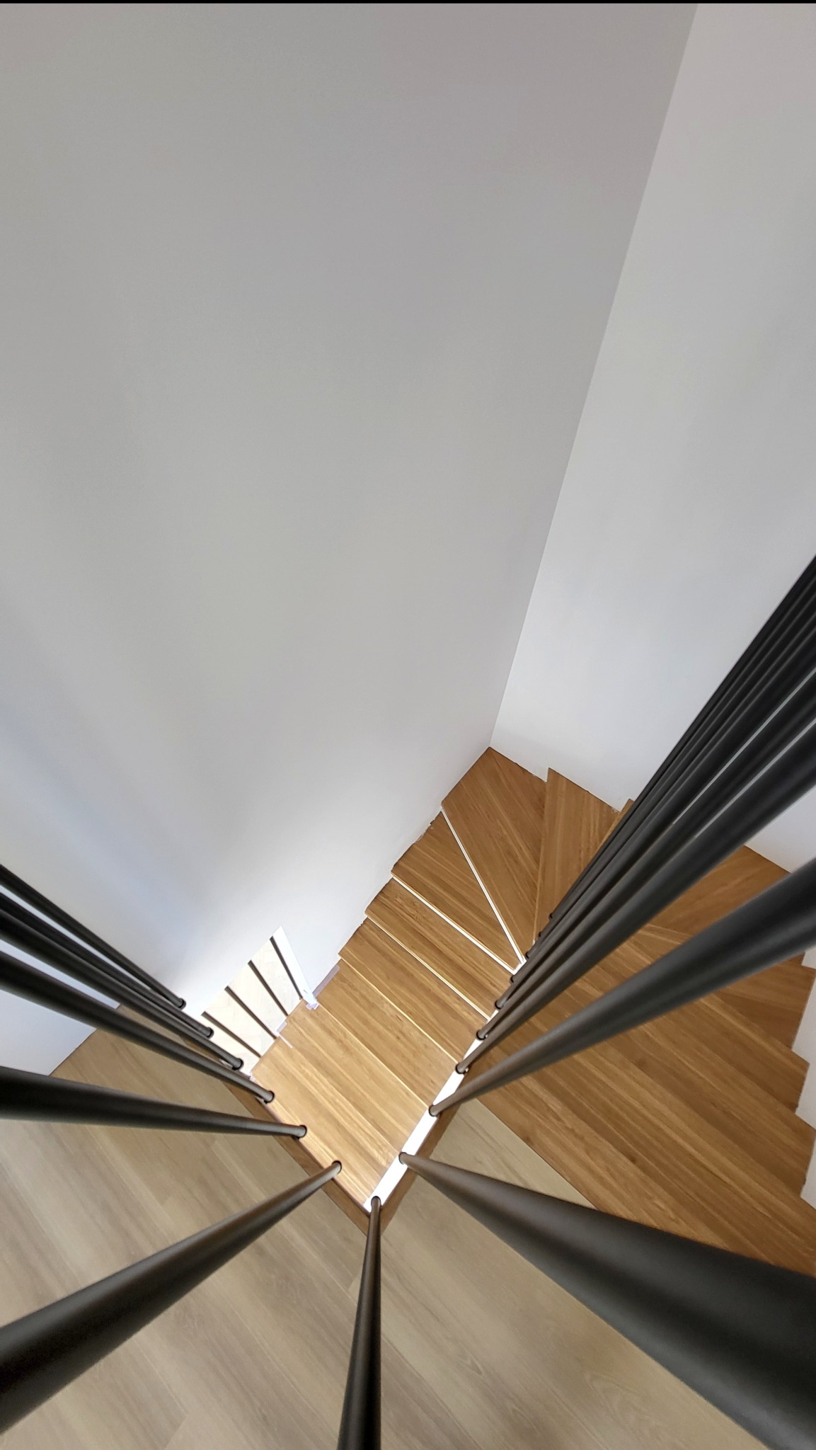 Nowoczesne schody z drewnianymi stopniami i czarnymi, stalowymi poręczami, widziane z góry, tworzące geometryczny wzór. Minimalistyczny design z kontrastem materiałów.