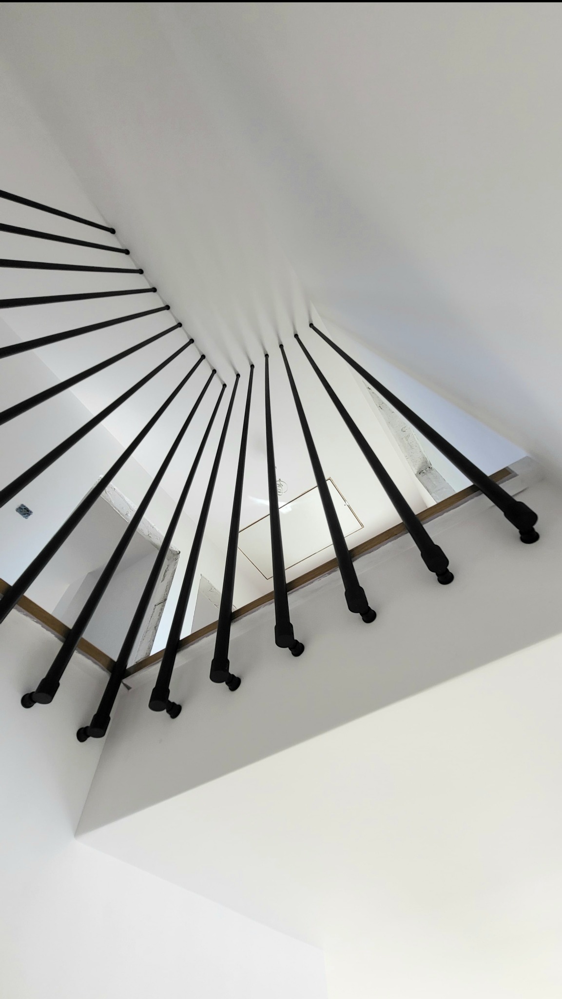 Nowoczesna balustrada schodowa z czarnych, stalowych rurek mocowanych do boku stopnia i sufitu, tworząca minimalistyczny wzór na tle białych ścian.