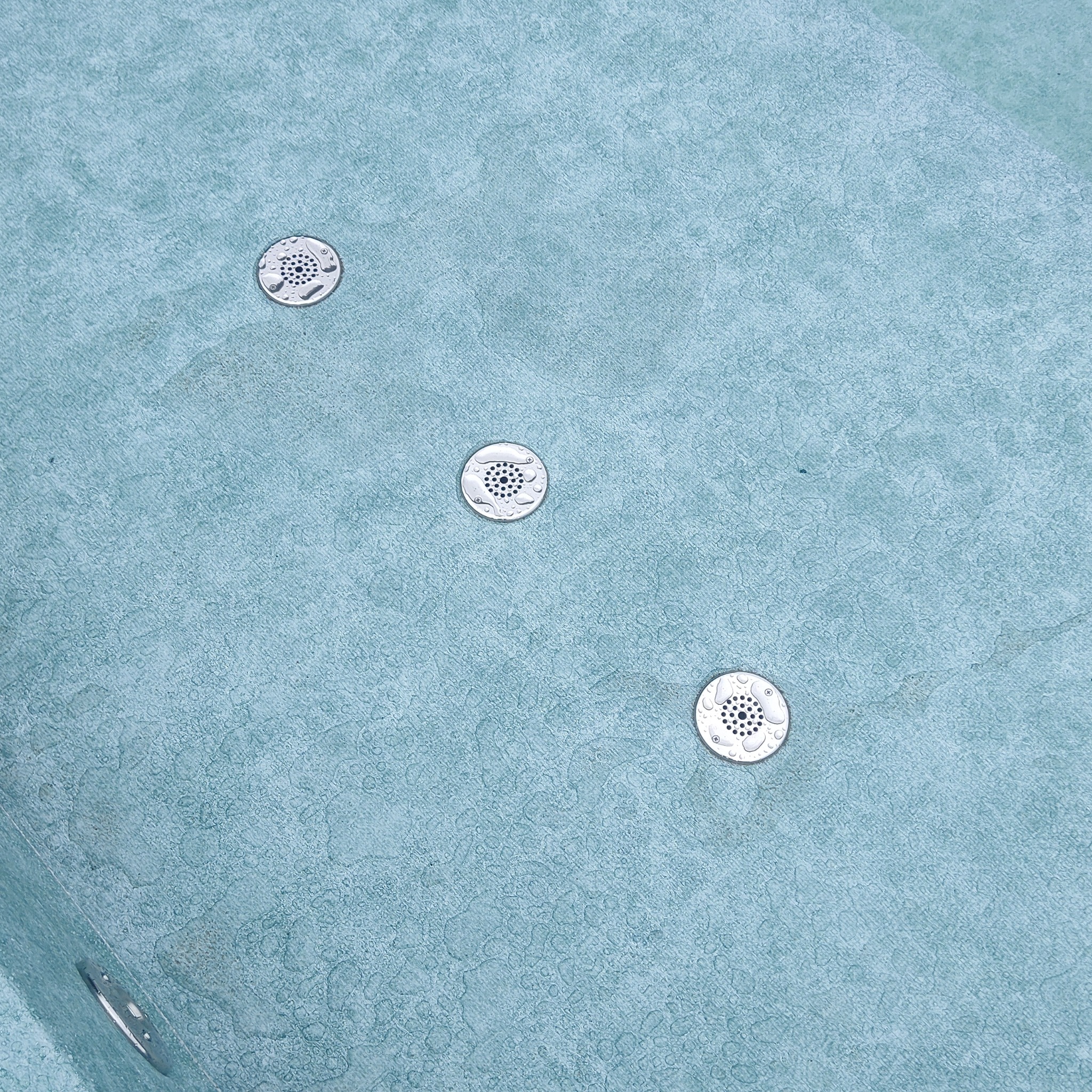 Błękitna powierzchnia wanny z hydromasażem z trzema metalowymi dyszami, pokryta kroplami wody.