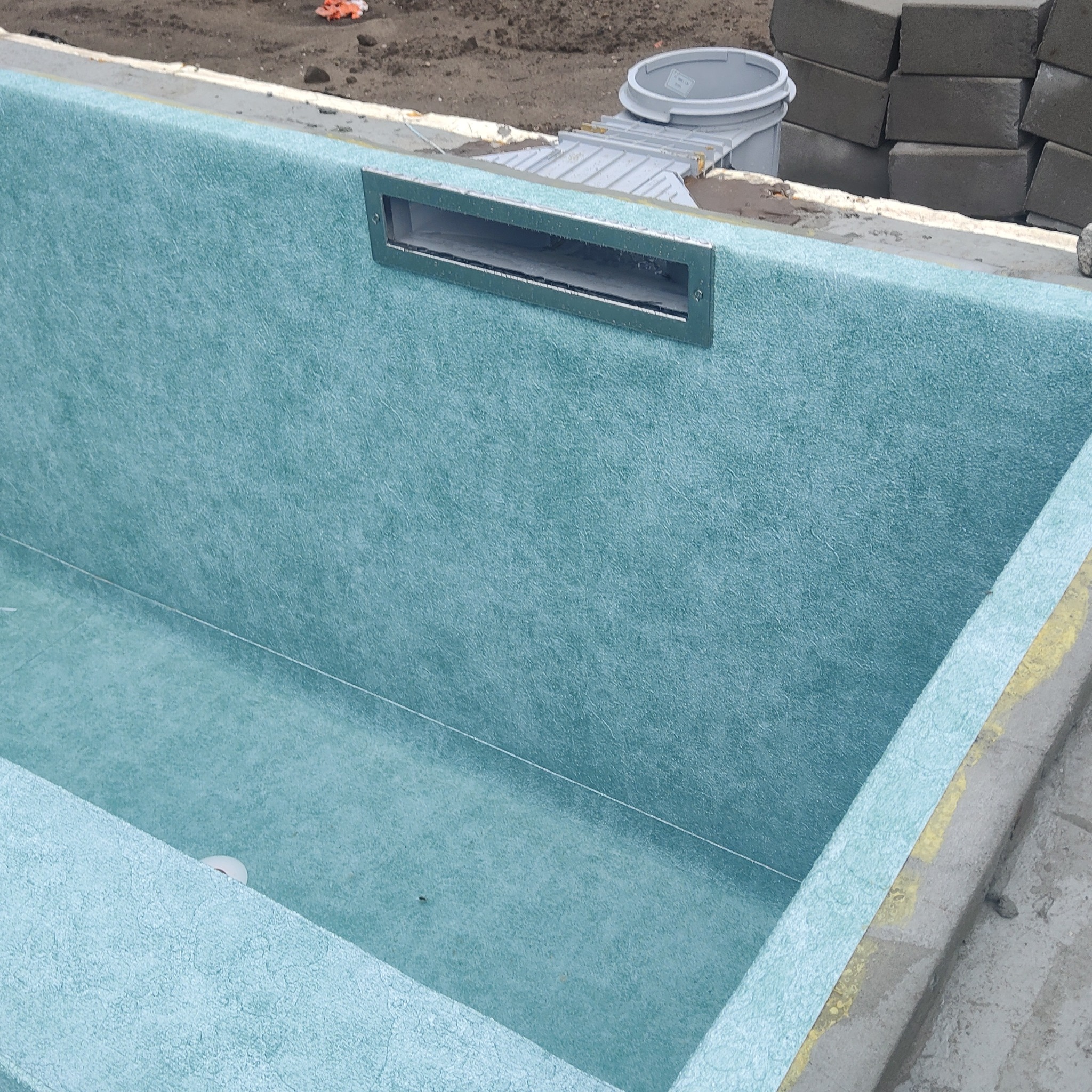 Wnętrze basenu wyłożone jasnoniebieską folią, z zamontowanym skimmerem. Na zewnątrz widoczne bloczki betonowe i wiadro.