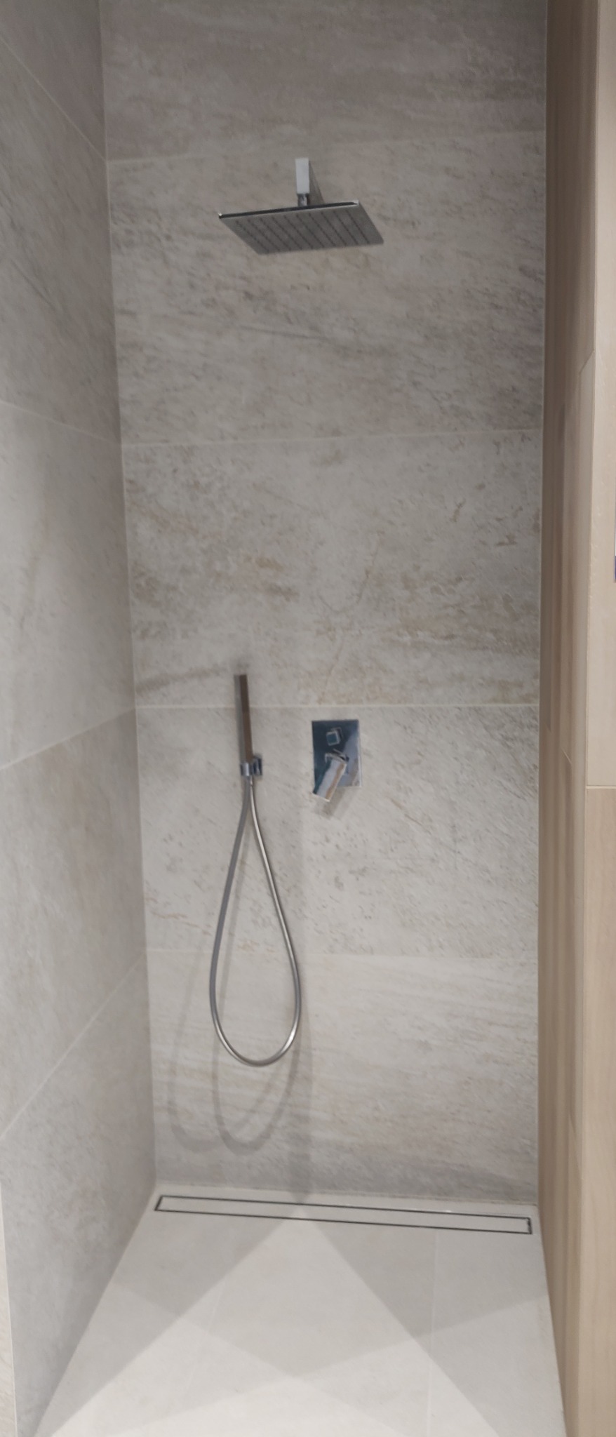 Nowoczesny prysznic z deszczownicą, marmurowymi płytkami i minimalistycznym odpływem liniowym.