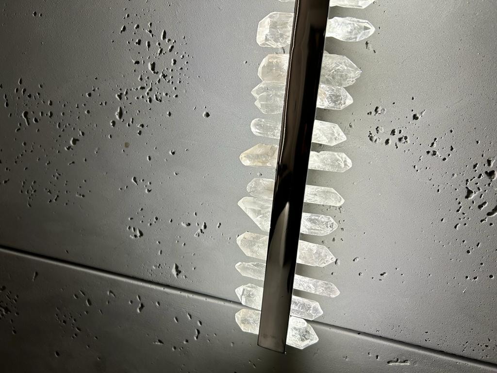 Ściana z szarego betonu z dekoracyjną, pionową listwą oświetleniową z metalu i kryształów, oświetlona od tyłu.