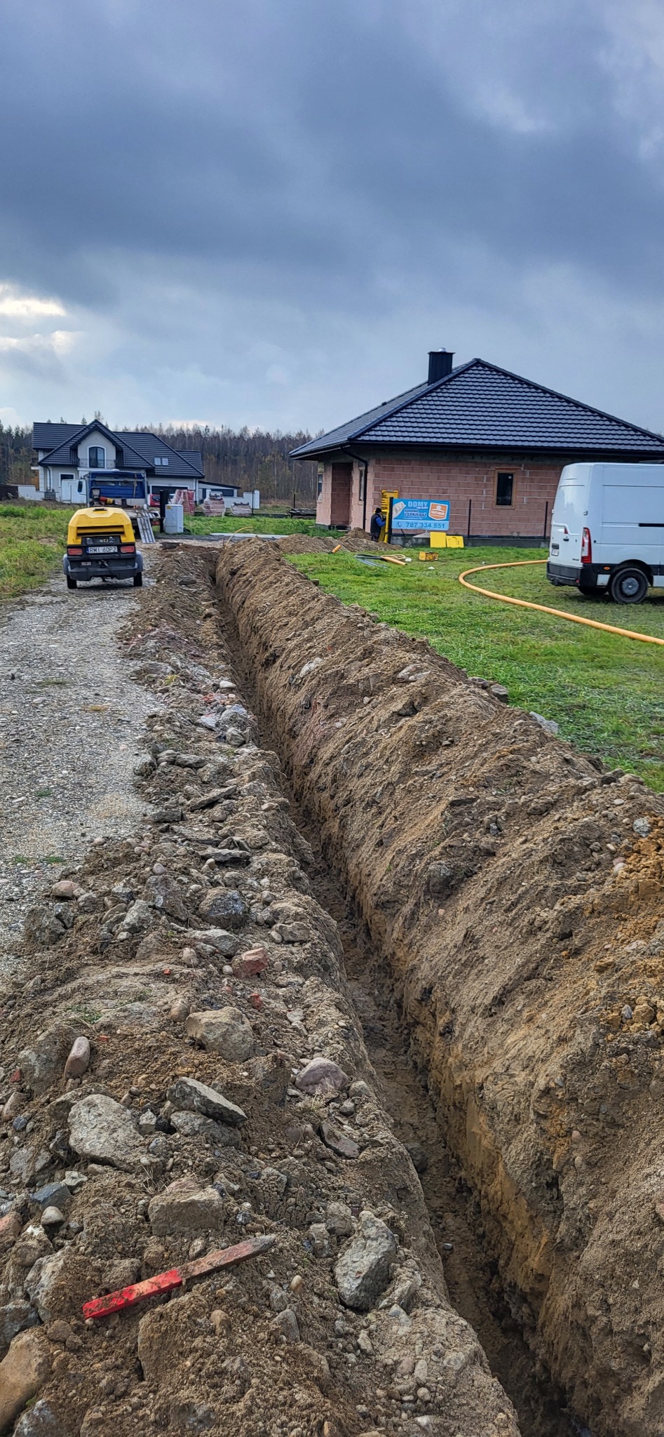 Wykop pod fundamenty na działce z częściowo wybudowanym domem z bloczków.