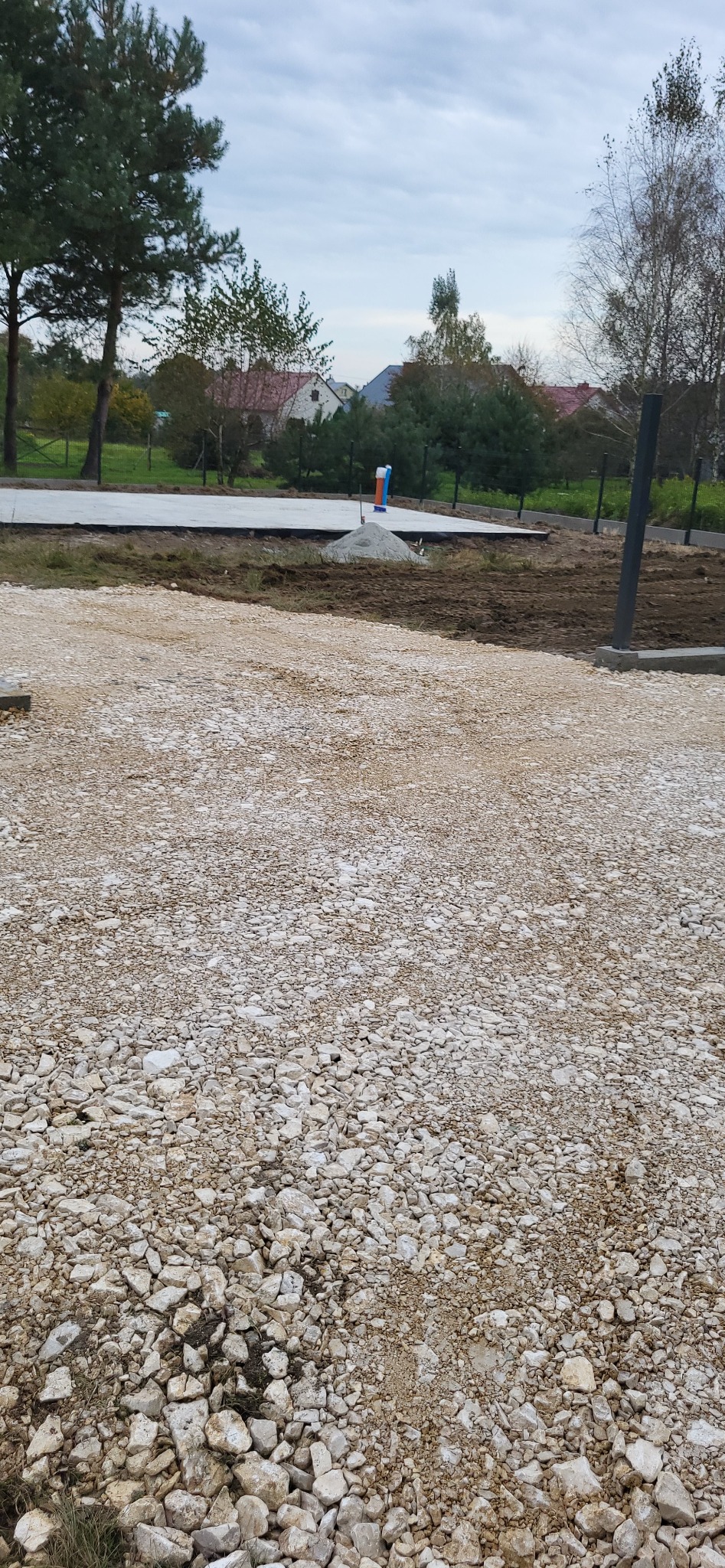 Przygotowany teren pod budowę z widocznym betonowym fundamentem, stertą piasku i wystającą rurą instalacyjną.