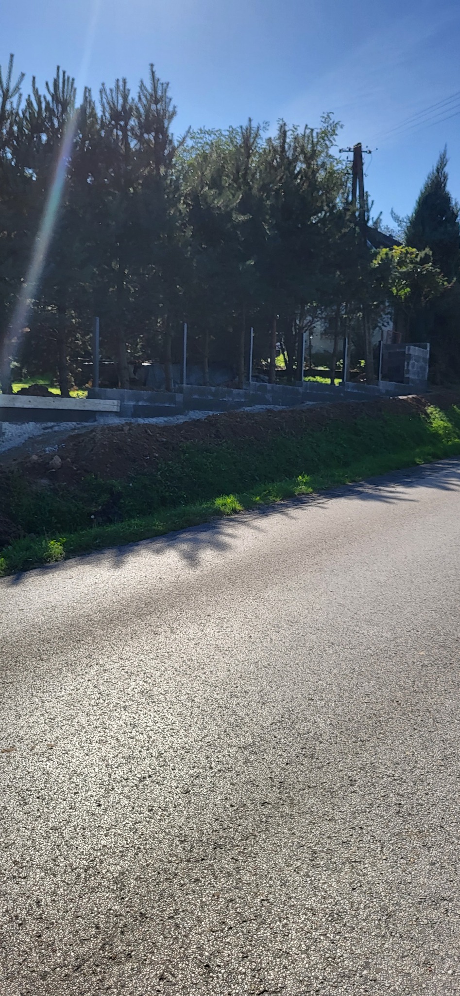 Wykop pod fundamenty, widoczne zbrojenia i betonowe bloczki na tle drzew i błękitnego nieba.