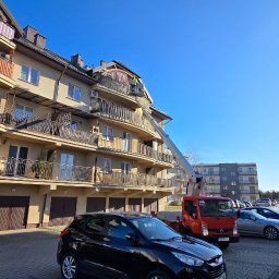 High-Work - Pracownik na podnośniku koszowym przy dachu budynku wielorodzinnego z balkonami, prawdopodobnie wykonuje prace dekarskie.