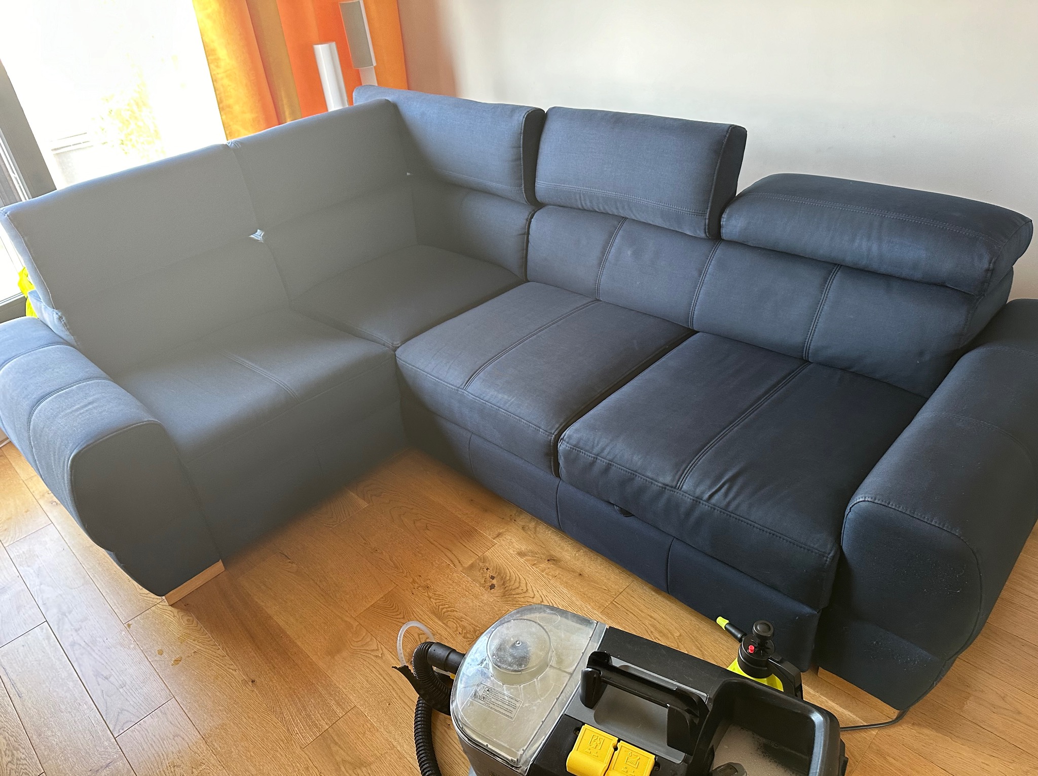 Narożnik z ciemnej tkaniny z regulowanymi zagłówkami oraz urządzenie do ekstrakcyjnego czyszczenia tapicerki na parkiecie.