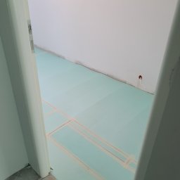 Coobmix - Przygotowanie podłoża pod podłogę: płyty izolacyjne z taśmą na wylewce, widok zza futryny drzwiowej.