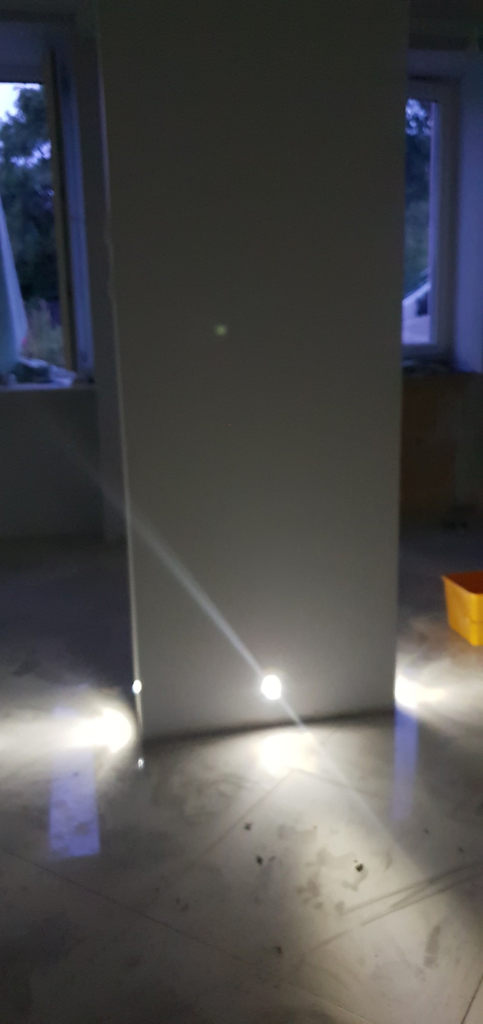 Świeżo postawiona ścianka działowa z płyt gipsowo-kartonowych w trakcie prac wykończeniowych, widoczne ślady szpachlowania na podłodze i w dolnej części ściany, dwa okna w tle.