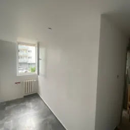 Pokój po świeżym malowaniu ścian na biało, z nową podłogą z szarych płytek imitujących marmur, widoczne przygotowania do montażu oświetlenia sufitowego.