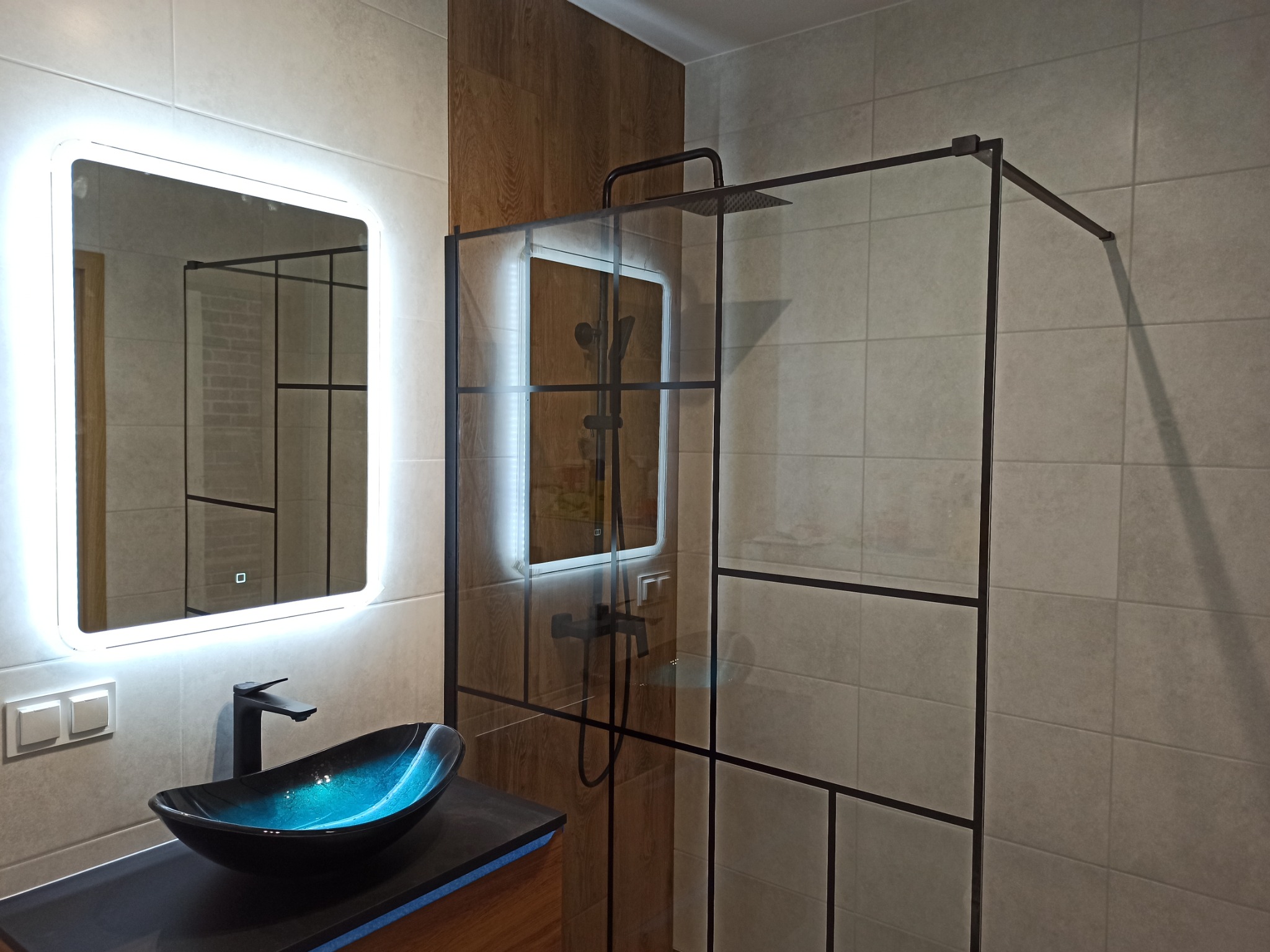 Nowoczesna łazienka z kabiną prysznicową typu walk-in z czarnymi profilami, umywalką nablatową w odcieniach czerni i turkusu oraz lustrem z podświetleniem LED.