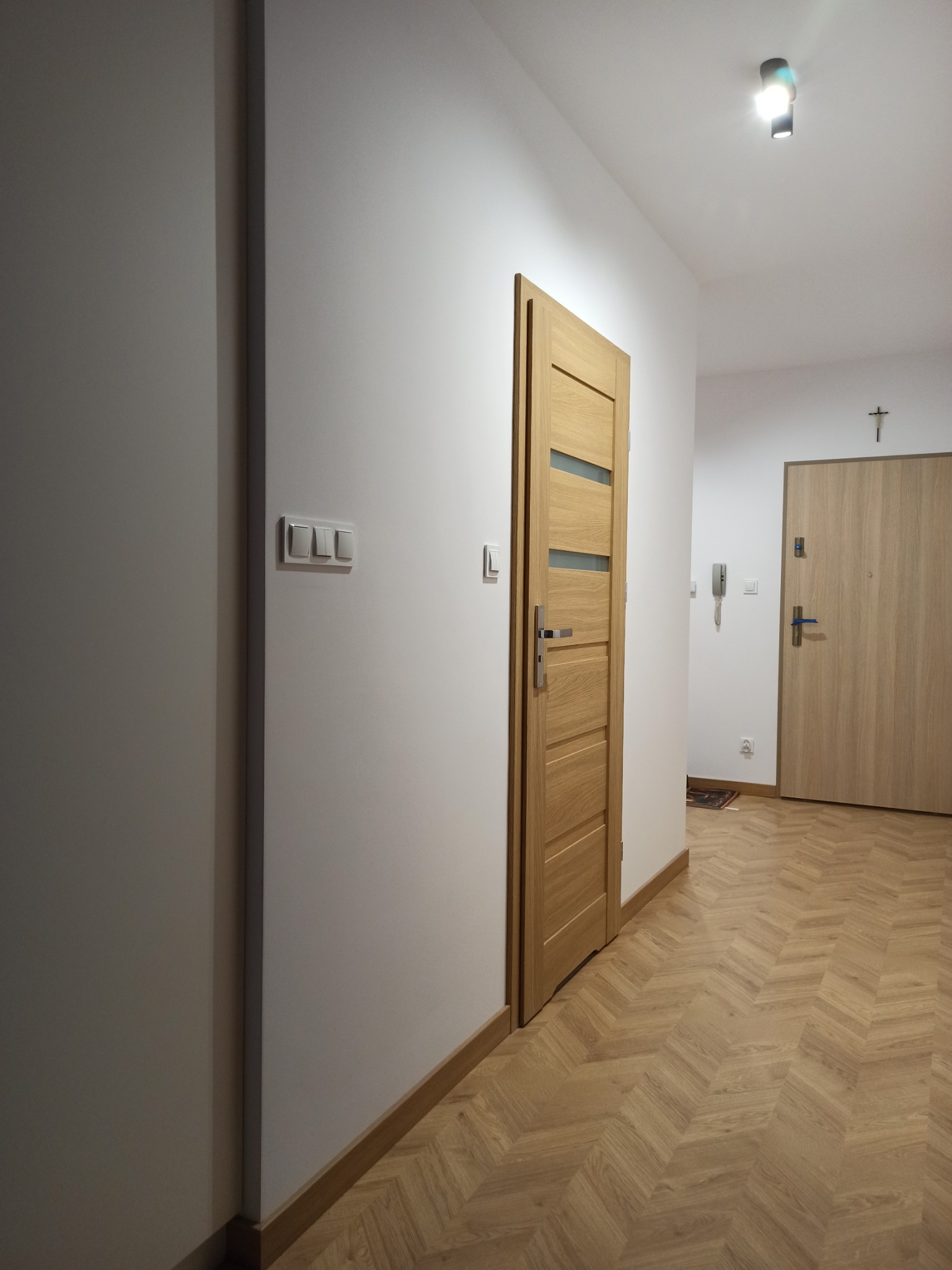 Jasny korytarz po remoncie z parkietem w jodełkę, dwiema parami drzwi z przeszkleniami i gładkimi, białymi ścianami.