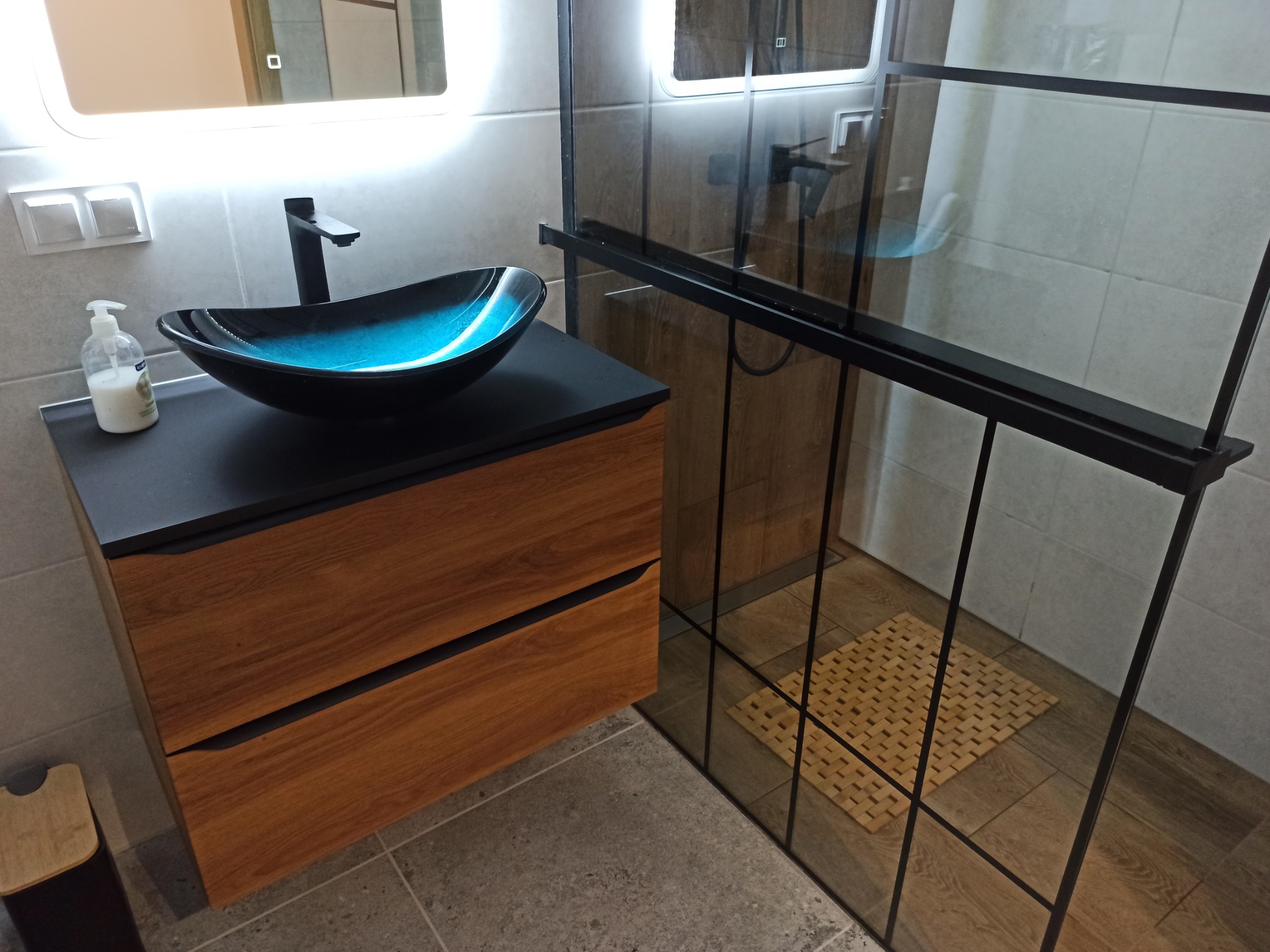 Nowoczesna łazienka z umywalką w kształcie misy w odcieniach niebieskiego, drewnianą szafką pod umywalką i kabiną prysznicową z czarnymi ramami.