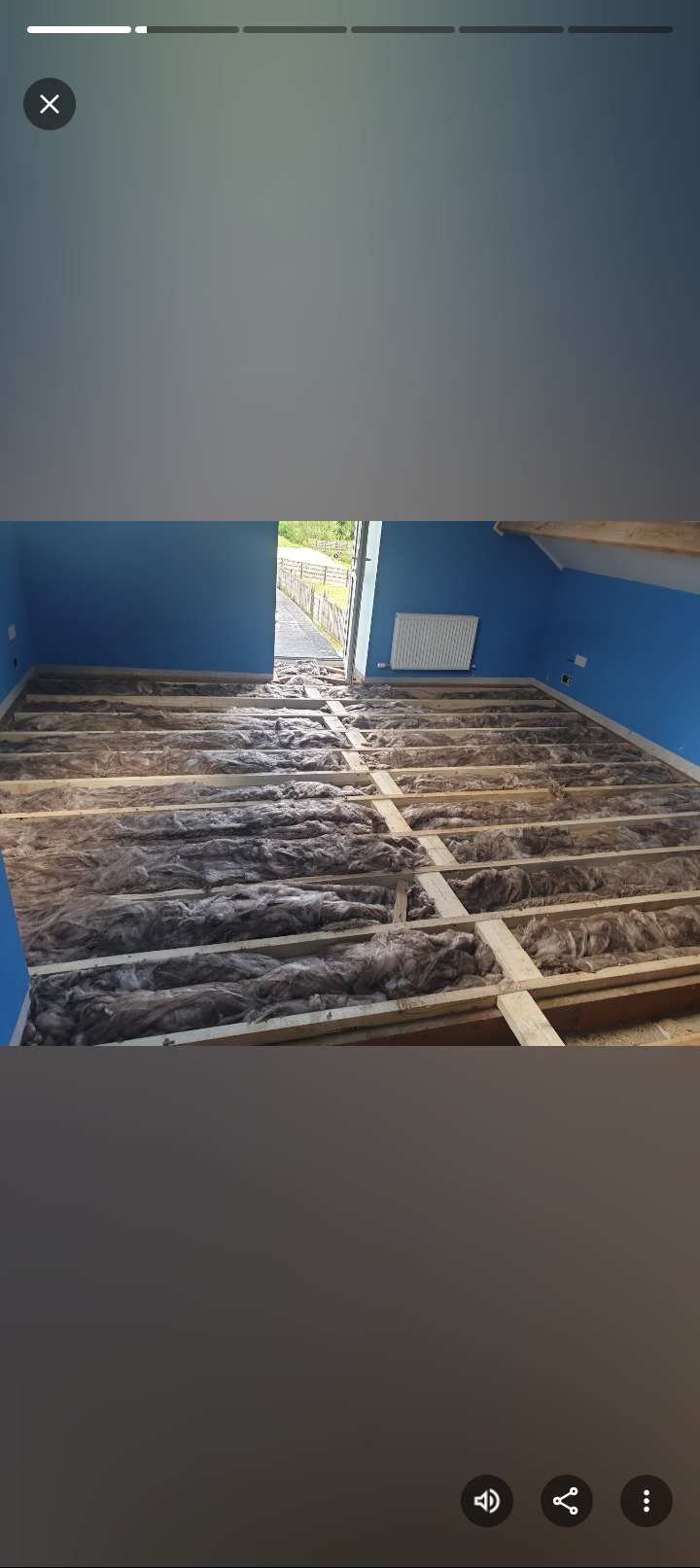 Poddasze z ociepleniem w trakcie prac: drewniana konstrukcja wypełniona wełną mineralną, niebieskie ściany, widok na zewnątrz przez otwarte drzwi.