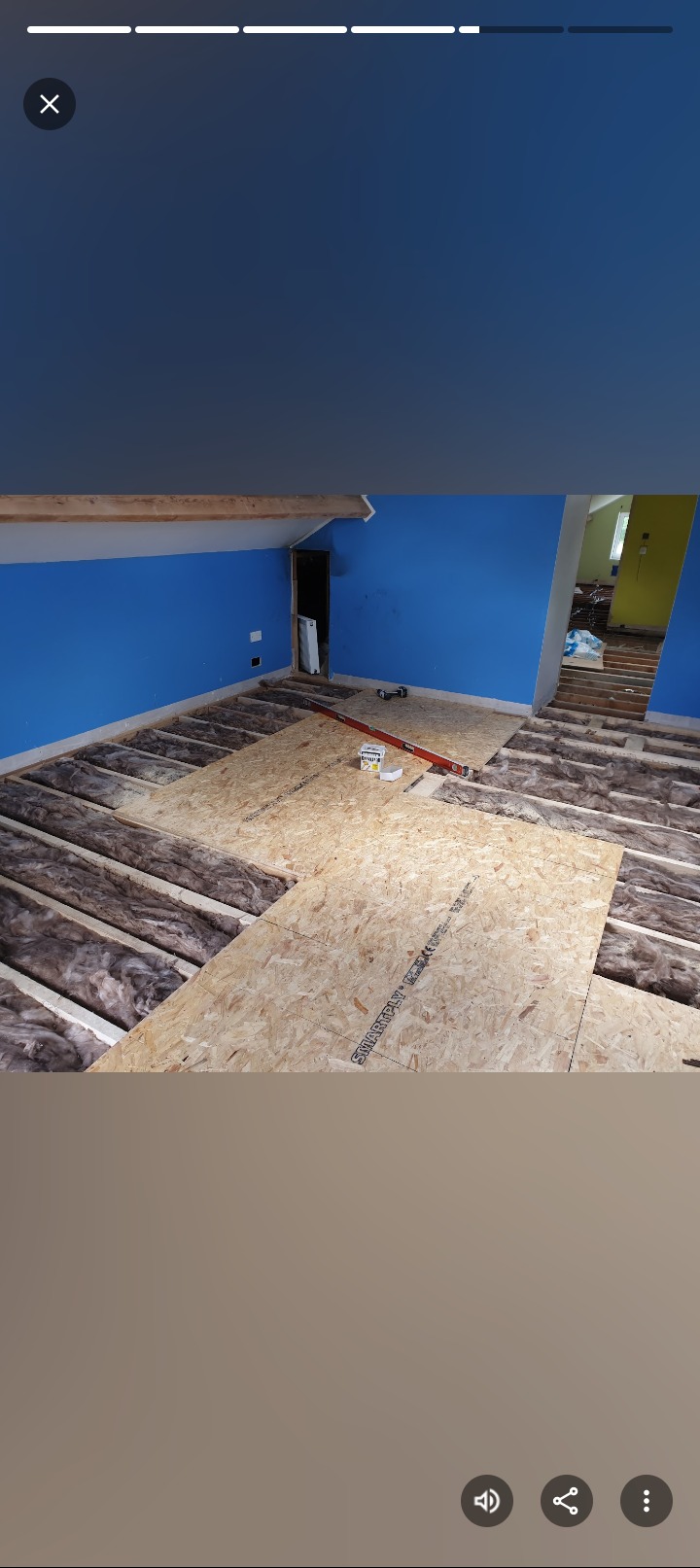 Poddasze z ociepleniem wełną mineralną i płytami OSB, poziomica, niebieska ściana, widok z góry, etap prac wykończeniowych.