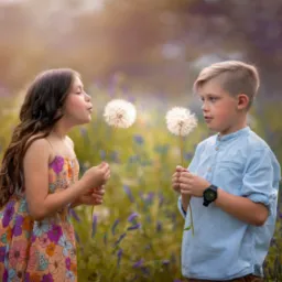 Dziewczynka w kwiecistej sukience i chłopiec z zegarkiem trzymają dmuchawce na łące w ciepłym, rozmytym świetle.