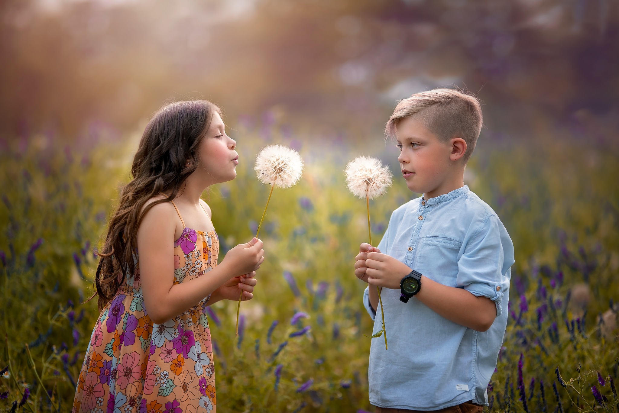 Dziewczynka w kwiecistej sukience i chłopiec z zegarkiem trzymają dmuchawce na łące w ciepłym, rozmytym świetle.