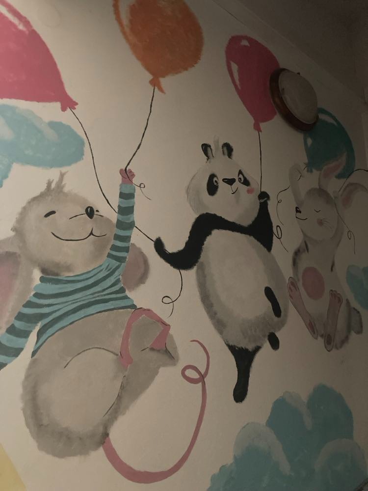 Malowidło ścienne w pokoju dziecięcym w Warszawie: uśmiechnięty mysz w niebieskiej koszulce, panda i królik unoszą się na balonach.