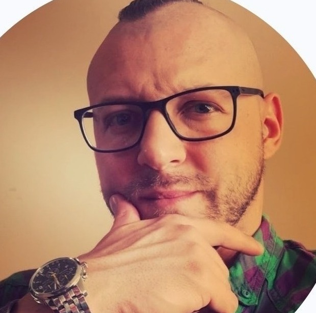 Portret mężczyzny z irokezem, w okularach z czarnymi oprawkami, w zielono-fioletowej koszuli w kratę, z zegarkiem na ręce, dotykającego brody