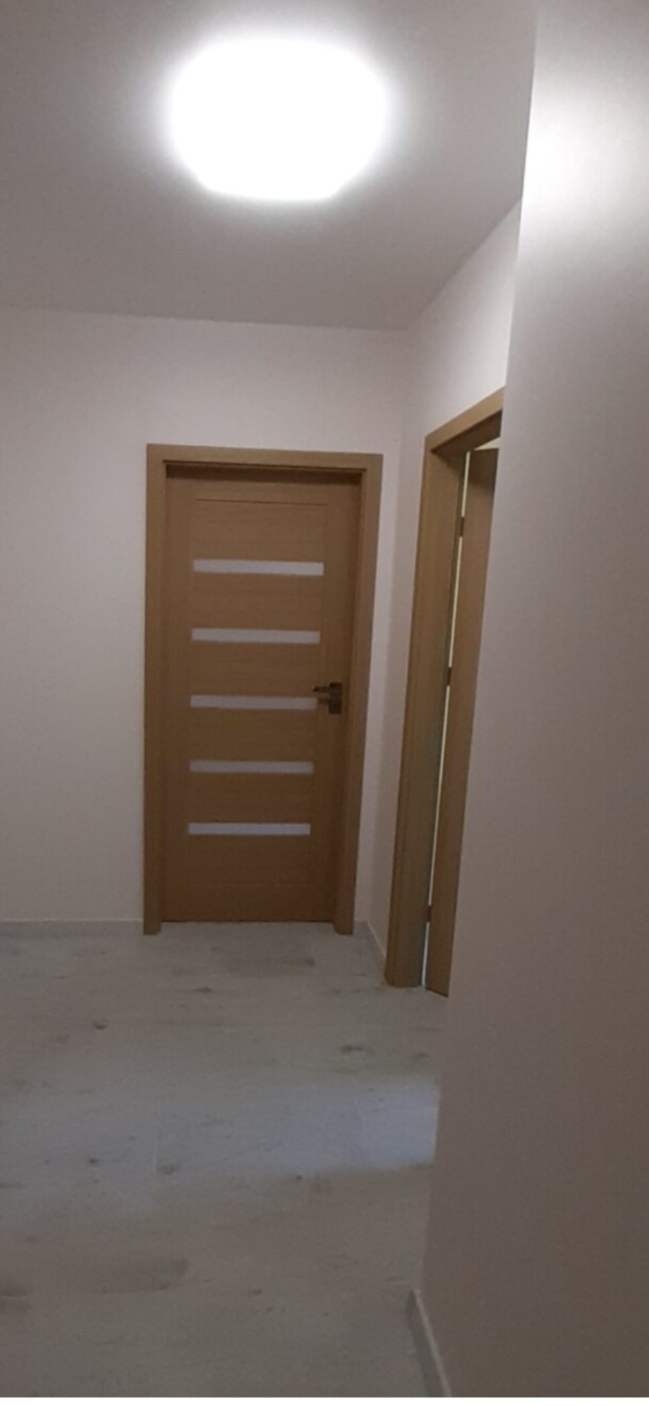 Wnętrze po odświeżeniu: widok na dwie zamontowane, drewniane drzwi z poziomymi przeszkleniami, jasne ściany i podłoga, oświetlenie sufitowe.