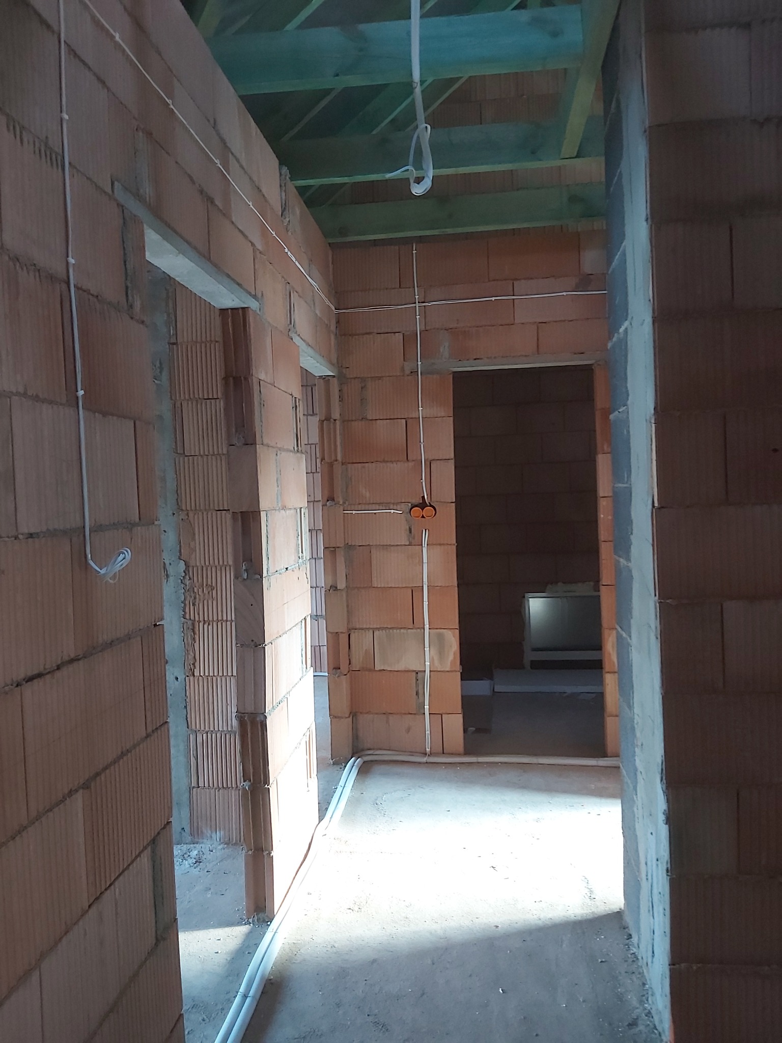 Wnętrze budynku w trakcie budowy z widocznymi przewodami elektrycznymi prowadzonymi po ścianach z cegły ceramicznej, puszkami instalacyjnymi i drewnianą konstrukcją stropu.