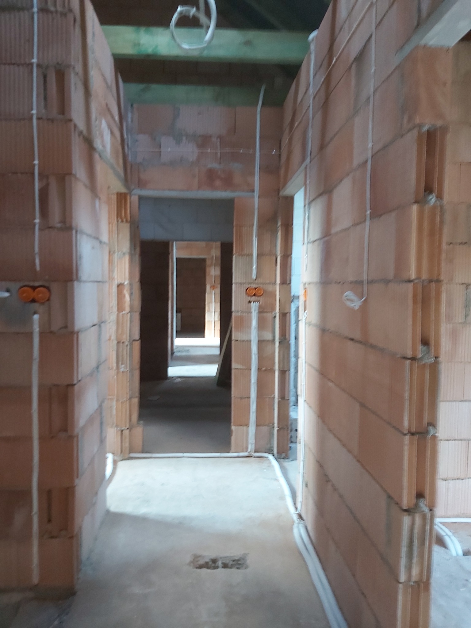 Wnętrze budynku w stanie surowym: widoczne ściany z czerwonej cegły, instalacje elektryczne w rurkach PCV prowadzone po ścianach i pod sufitem, puszki elektryczne zamontowane w ścianach, surowy...