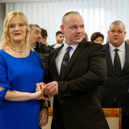 Martyna Baster - Photo - Para młoda trzymająca się za ręce podczas ceremonii ślubnej, w tle goście weselni i białe zasłony.