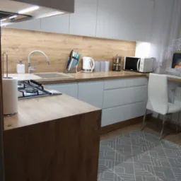 Jasna kuchnia z drewnianym blatem i białymi szafkami, widoczny narożny zlew, płyta gazowa, akcesoria kuchenne i szary dywan z geometrycznym wzorem.