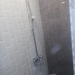 MegaBuD Viacheslav Sapko - Wykończona kabina prysznicowa z szarymi i białymi, prostokątnymi płytkami ułożonymi w cegiełkę. Widoczna chromowana bateria i deszczownica.