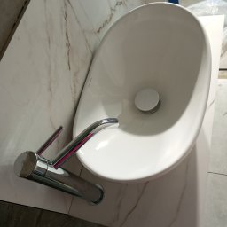 MegaBuD Viacheslav Sapko - Biała umywalka nablatowa z chromowaną baterią na blacie imitującym marmur. Widok z góry, ukośny. Ukończona instalacja w łazience.