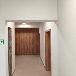 MegaBuD Viacheslav Sapko - Korytarz po remoncie z drewnianą zabudową szafy wnękowej i ościeżnicami. Na ścianie znak ewakuacyjny. Podłoga wyłożona płytkami. Widok z perspektywy.