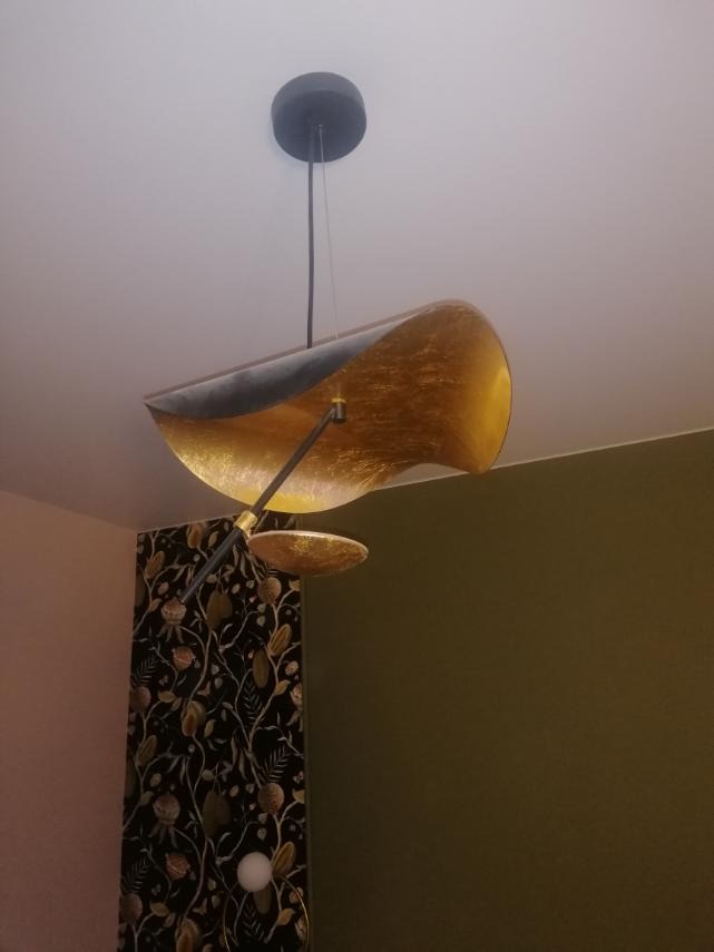 Nowoczesna lampa wisząca z elementami złota, na tle ściany z wzorzystą tapetą i gładkiej ściany w odcieniach zieleni i różu. Oryginalne oświetlenie wnętrza.