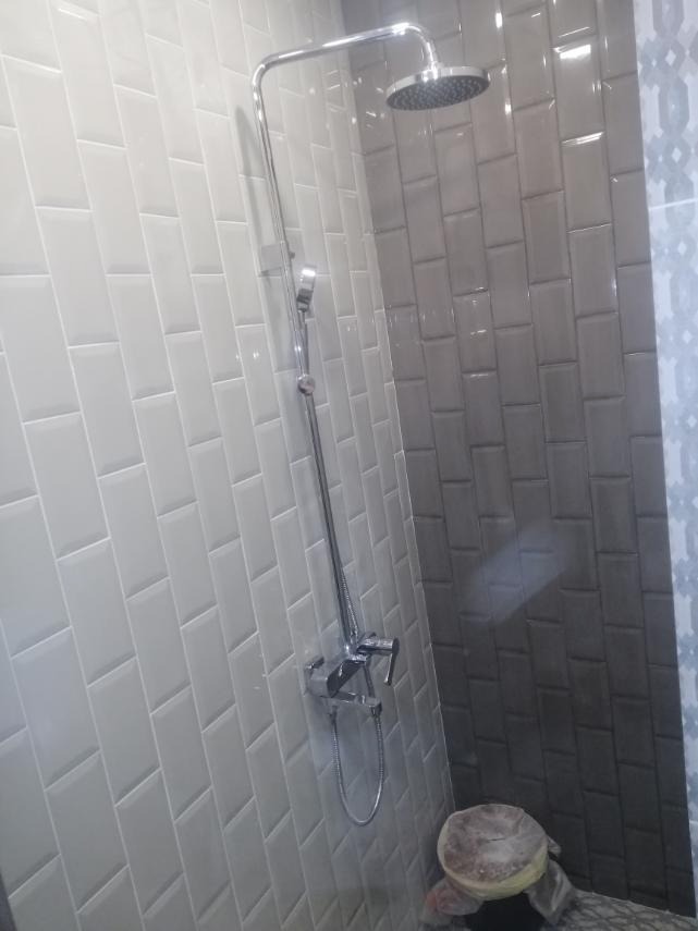 Wykończona kabina prysznicowa z szarymi i białymi, prostokątnymi płytkami ułożonymi w cegiełkę. Widoczna chromowana bateria i deszczownica.